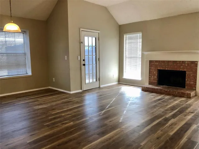 an empty room with wooden floor fireplace and windows