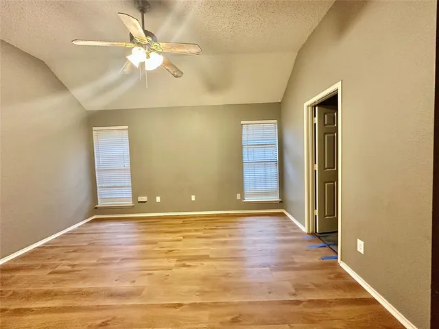 an empty room with wooden floor fan and windows