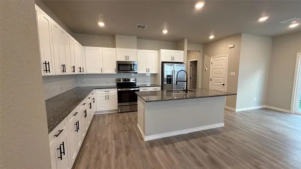 a kitchen with stainless steel appliances granite countertop a refrigerator a stove top oven a sink and dishwasher with wooden floor