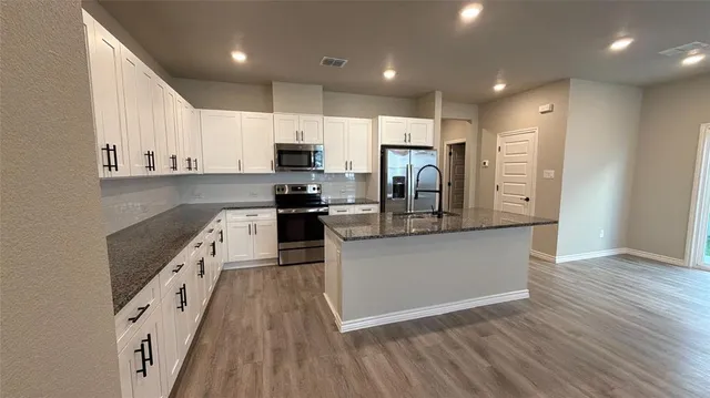 a kitchen with stainless steel appliances granite countertop a refrigerator a stove top oven a sink and dishwasher with wooden floor