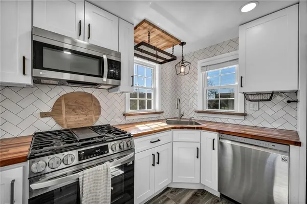 a kitchen with granite countertop a stove top oven a sink dishwasher and white cabinets with wooden floor