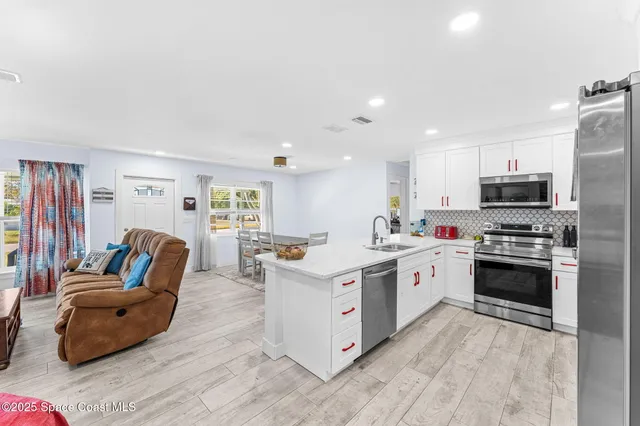 a large white open kitchen with stainless steel appliances granite countertop a stove oven a sink dishwasher and a refrigerator with wooden floor