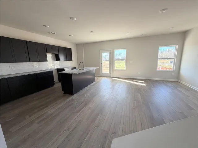 a living room with stainless steel appliances kitchen island granite countertop a sink and wooden floor