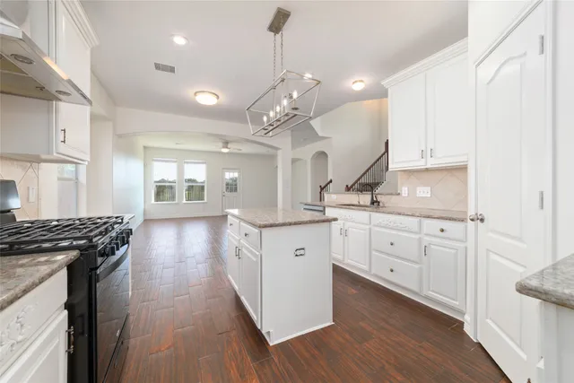 a large kitchen with granite countertop a stove top oven a sink a dining table and chairs with wooden floor