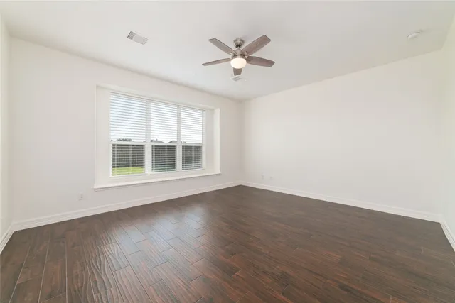 an empty room with wooden floor fan and windows