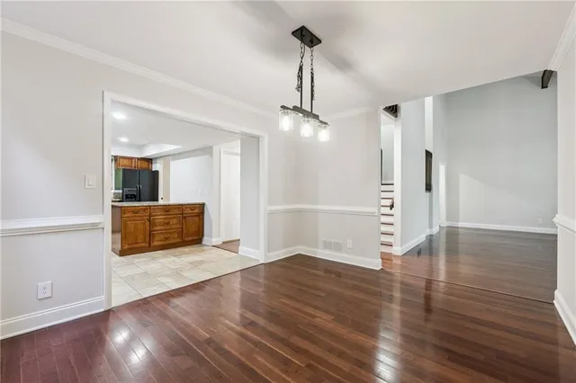a view of an empty room with wooden floor and a kitchen