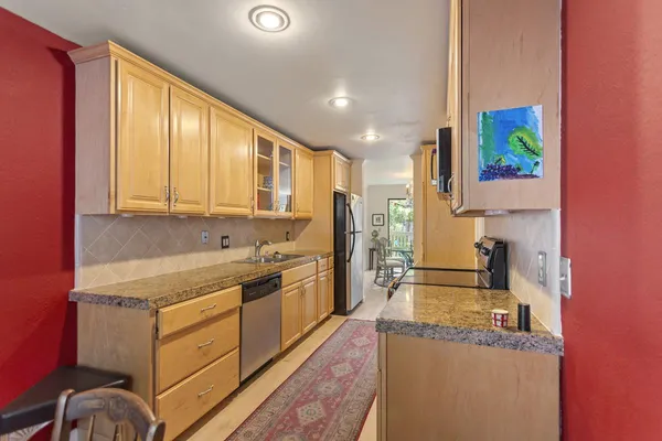 a kitchen with stainless steel appliances granite countertop a refrigerator a stove top oven and a sink with large cabinets