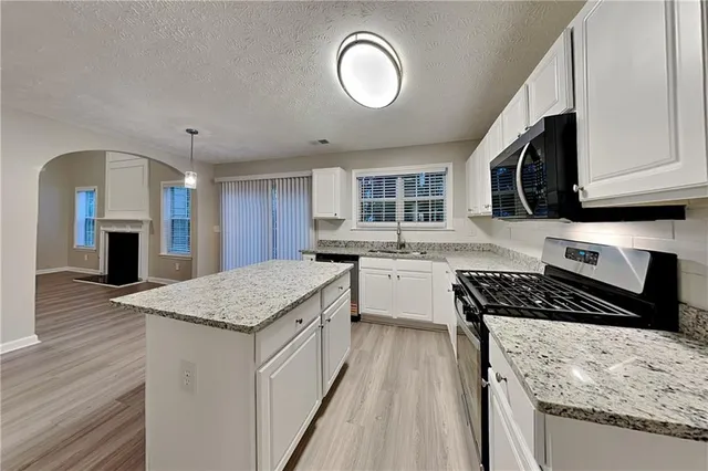 a kitchen with granite countertop cabinets a sink a stove and wooden floors