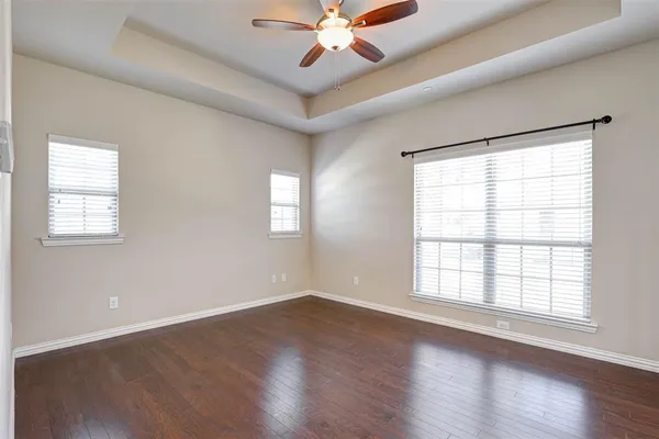 an empty room with wooden floor chandelier fan and windows