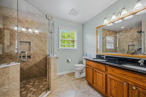 a spacious bathroom with a granite countertop sink a toilet a mirror and shower