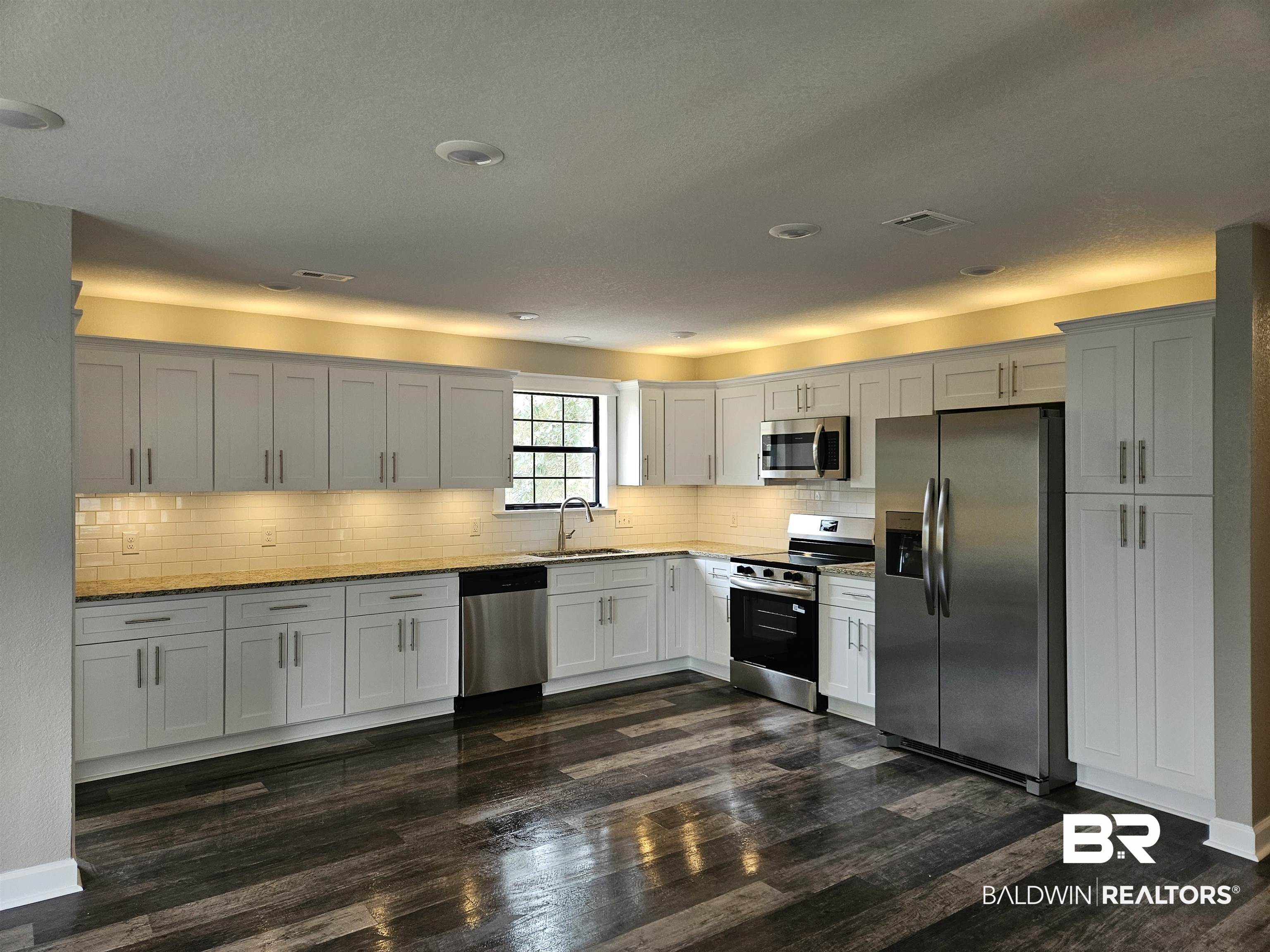 138 Wicker Way Daphne, AL 36526 - Photo 6 of 32 Kitchen featuring stainless steel appliances, white cabinetry, light stone countertops, dark wood finished floors, and decorative backsplash