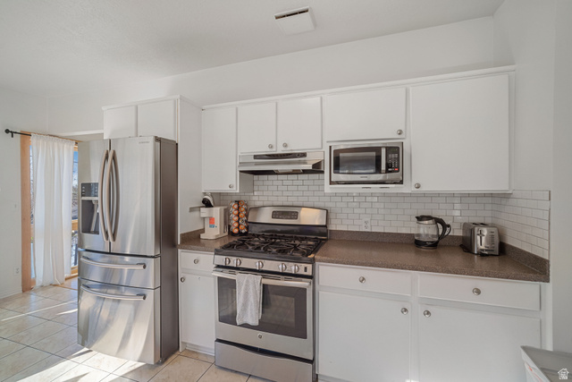 4426 South 3035 East Holladay, UT 84124 - Photo 7 of 49 Kitchen with stainless steel appliances, dark countertops, light tile patterned floors, white cabinets, and under cabinet range hood