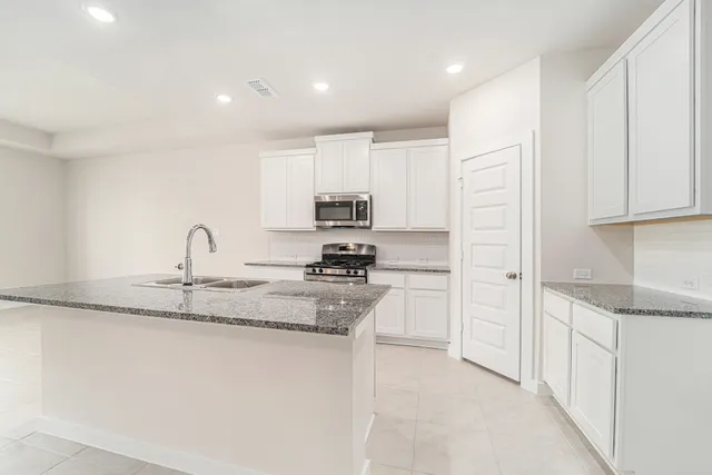 a kitchen with kitchen island granite countertop a sink white cabinets and stainless steel appliances