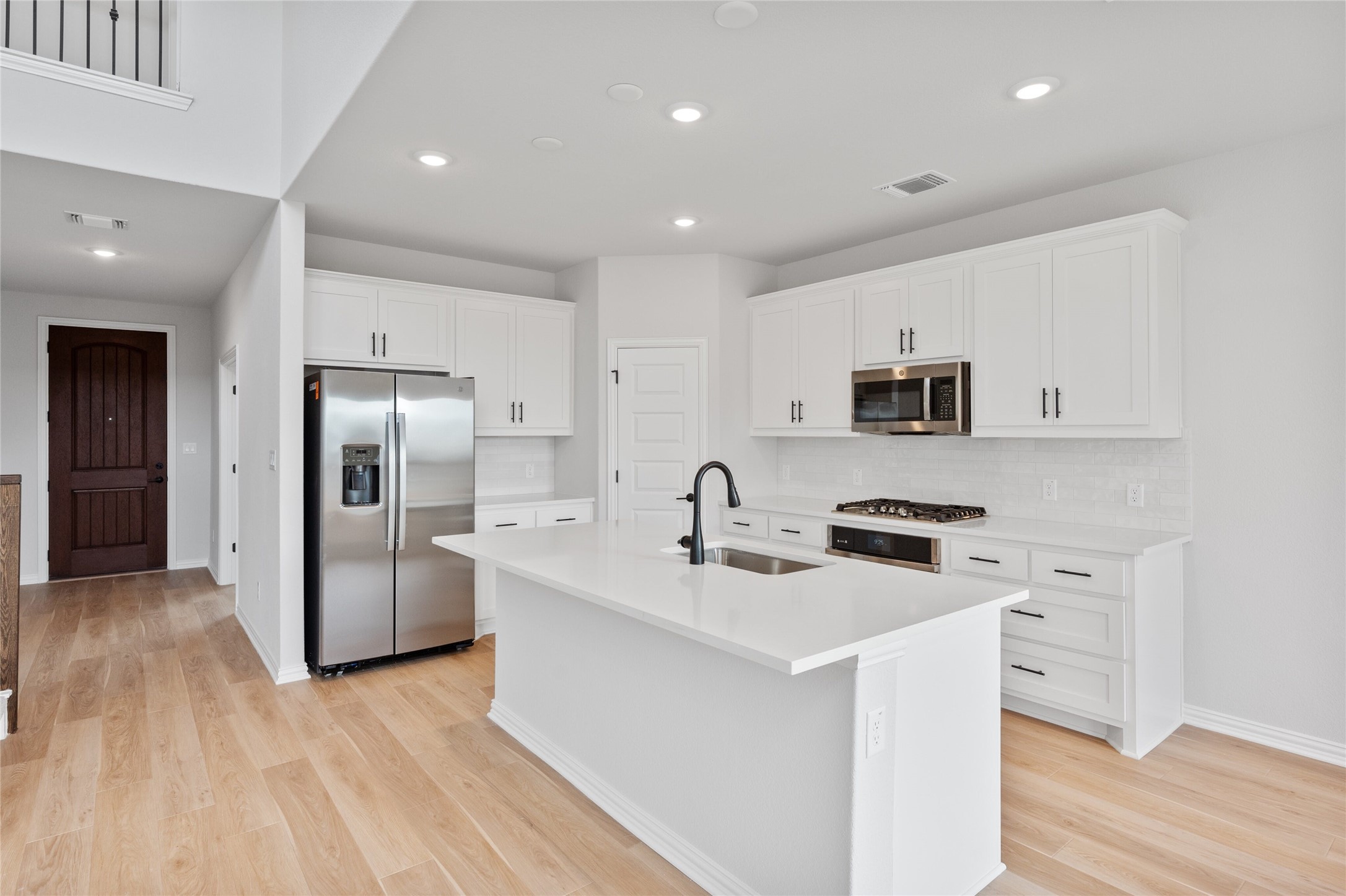 303 Fawn Riv Run Kyle, TX 78640 - Photo 11 of 32 Modern kitchen featuring a central island with an undermount sink, white shaker-style cabinetry, stainless steel appliances, and wood-finish flooring