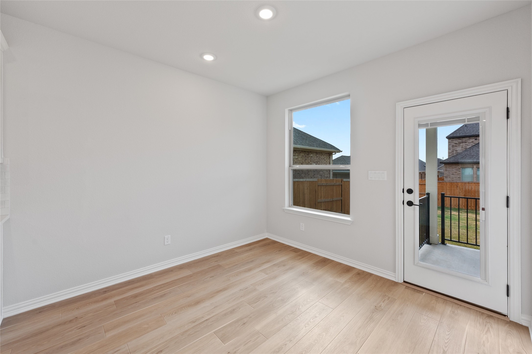 303 Fawn Riv Run Kyle, TX 78640 - Photo 12 of 32 Bright room featuring wood-finish flooring, recessed ceiling lighting, a large window, and a full-light exterior door with black hardware, opening to an outdoor patio with black iron railing