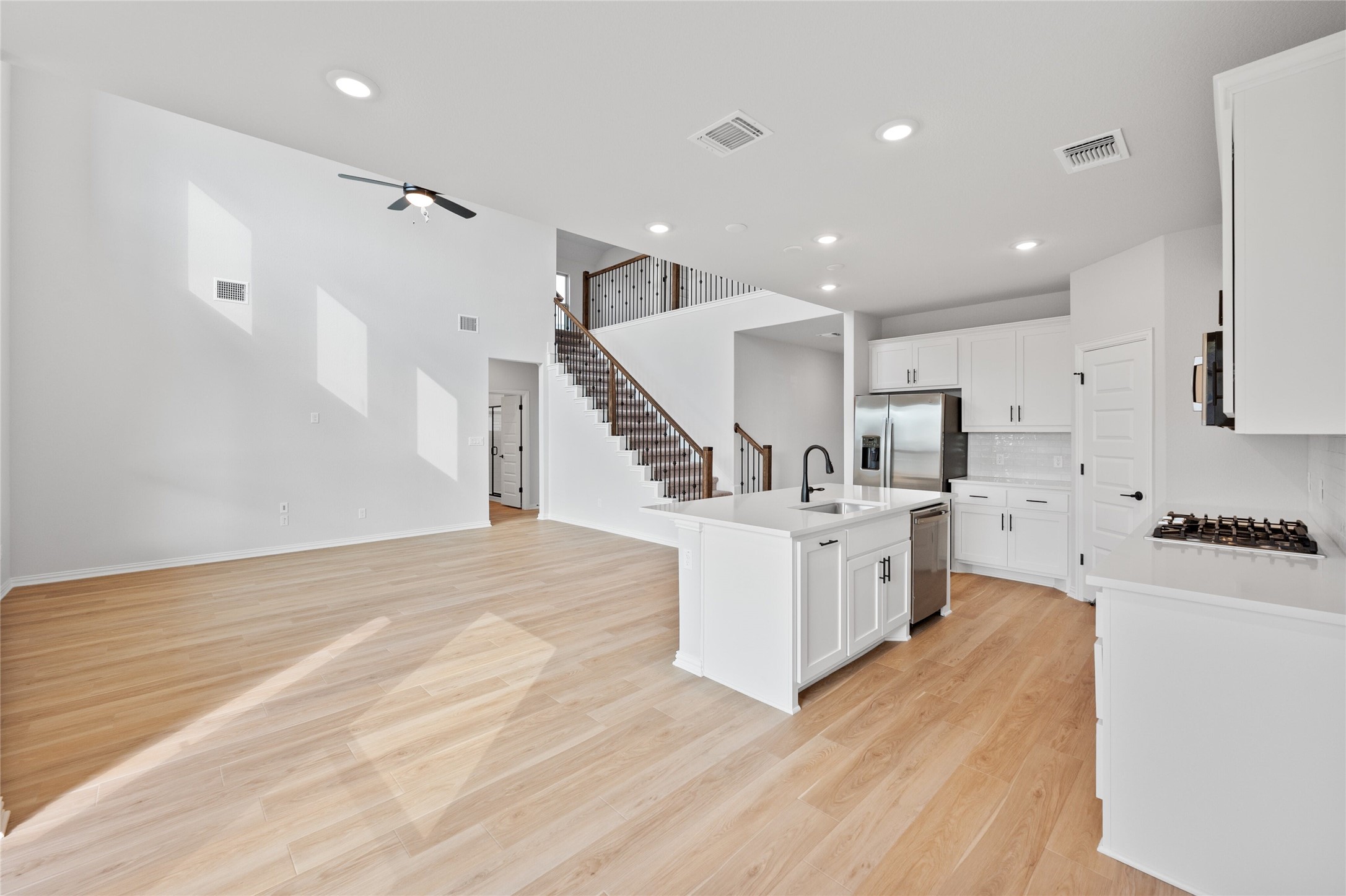 303 Fawn Riv Run Kyle, TX 78640 - Photo 13 of 32 Open-concept living area featuring light wood-finish flooring, recessed lighting, a modern ceiling fan, and a contemporary kitchen with white cabinetry and stainless steel appliances