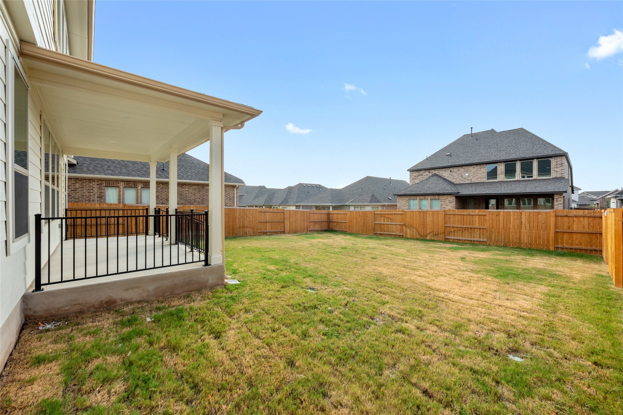 303 Fawn Riv Run Kyle, TX 78640 - Photo 32 of 32 Expansive backyard featuring a covered patio with a concrete surface and black metal railing, a perimeter wood privacy fence, and a large grass lawn