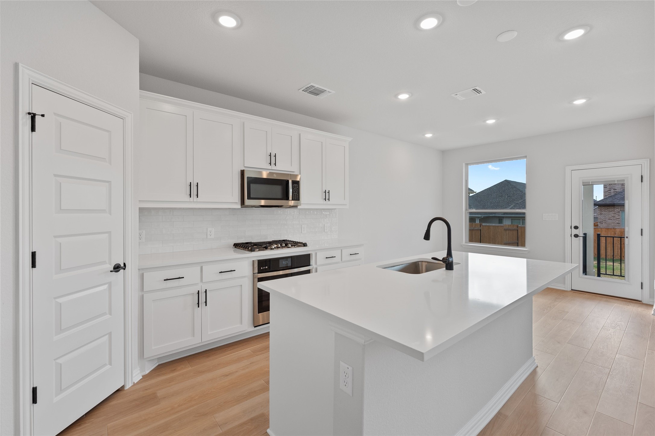 303 Fawn Riv Run Kyle, TX 78640 - Photo 8 of 32 Modern kitchen featuring white cabinetry, stainless steel appliances, a center island with sink and matte black faucet, and wood-finish flooring