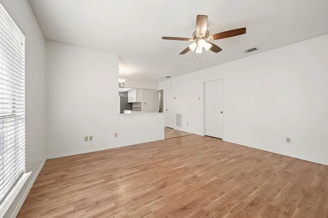 an empty room with wooden floor a ceiling fan a fireplace and windows