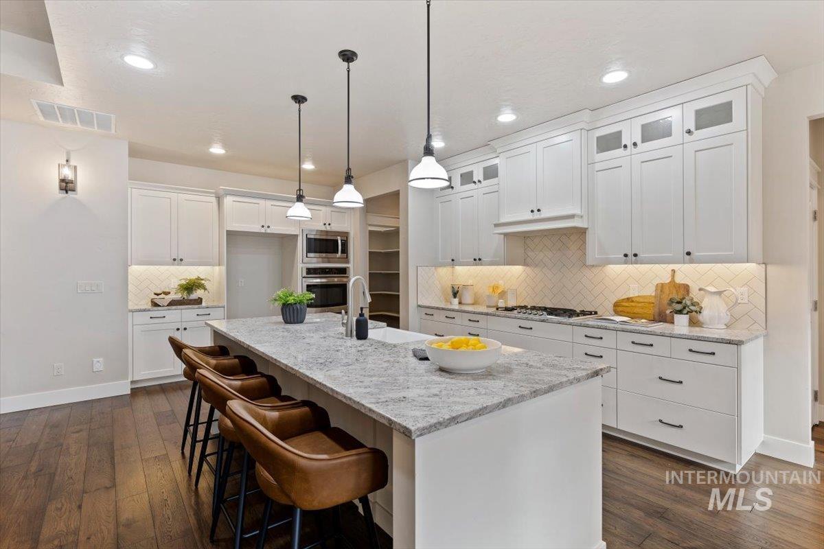 1366 North Waterbrook Way Star, ID 83669 - Photo 12 of 30 Kitchen featuring a breakfast bar, white cabinets, light stone counters, dark wood finished floors, and an island with sink