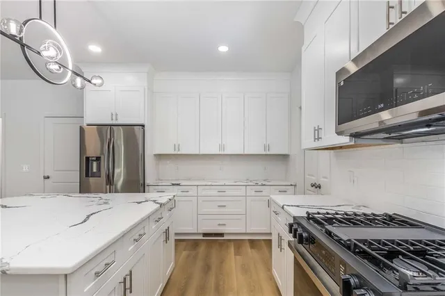 a large white kitchen with kitchen island a stove a sink dishwasher and white cabinets with wooden floor