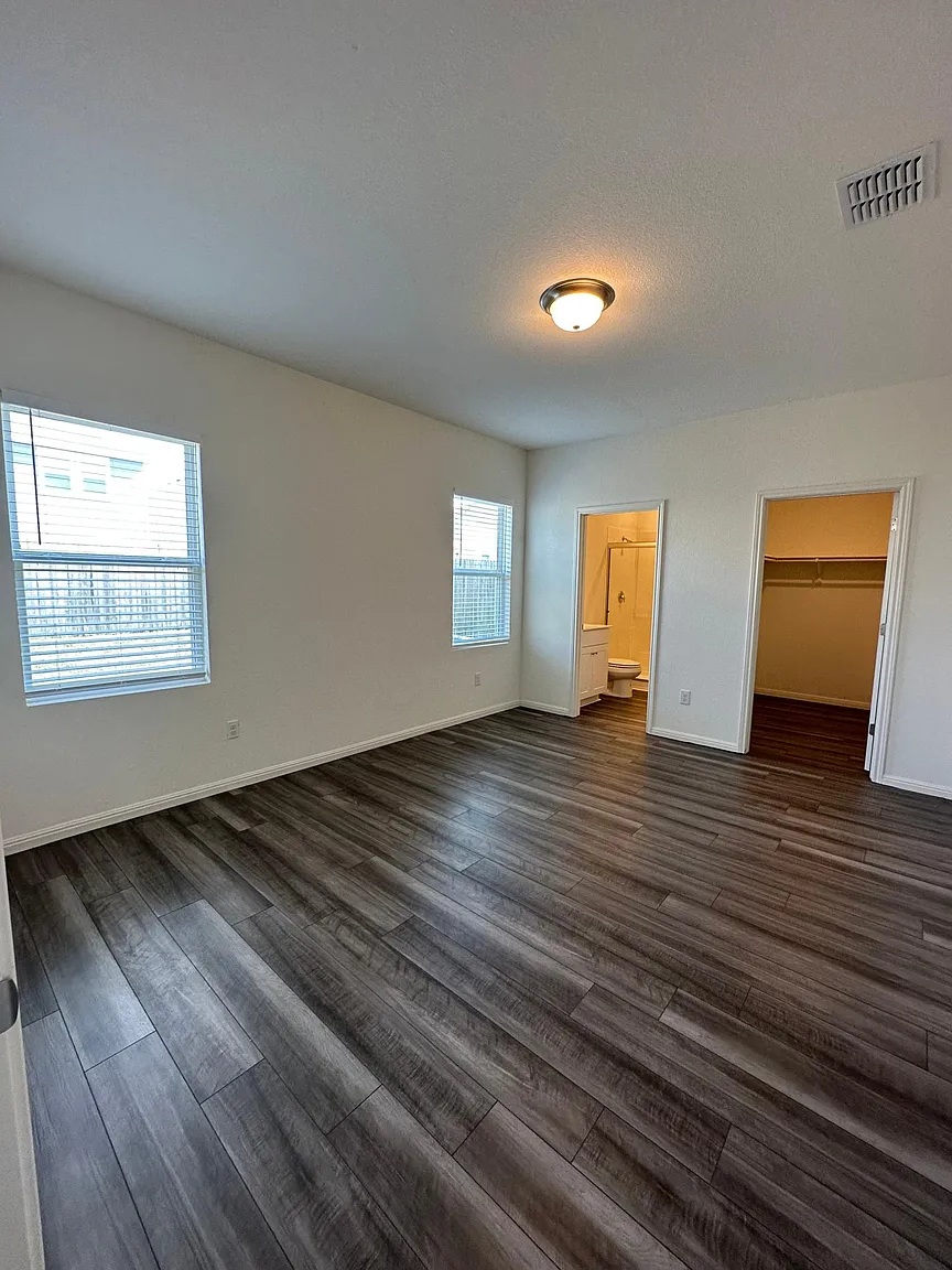 114 Aoudad Road Hutto, TX 78634 - Photo 13 of 22 Unfurnished bedroom featuring a walk in closet, dark wood-style flooring, and connected bathroom
