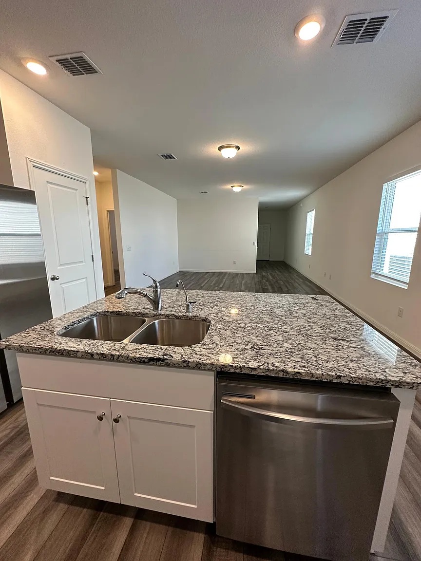 114 Aoudad Road Hutto, TX 78634 - Photo 4 of 22 Kitchen featuring stainless steel appliances, dark wood-style flooring, light stone counters, an island with sink, and white cabinets