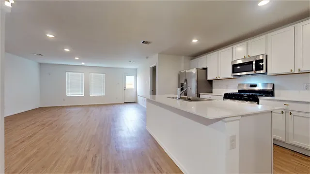 a kitchen with stainless steel appliances a sink a stove a microwave a refrigerator a white cabinets and wooden floor