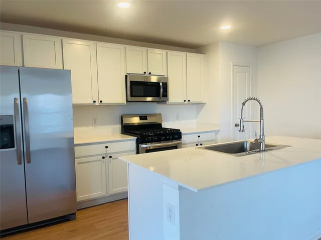 a kitchen with stainless steel appliances a sink a stove a microwave a refrigerator a sink and cabinets
