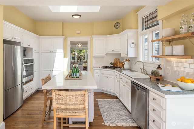 a large kitchen with stainless steel appliances kitchen island granite countertop a refrigerator a sink dishwasher a dining table and chairs with wooden floor