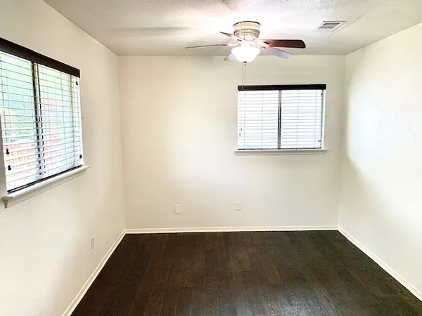 an empty room with wooden floor chandelier fan and windows
