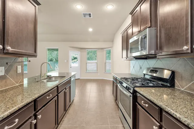 a kitchen with granite countertop stainless steel appliances a sink stove and cabinets