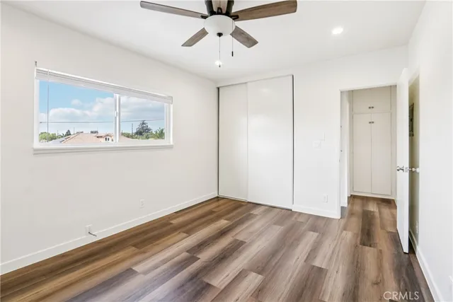 a view of an empty room with wooden floor and a ceiling fan