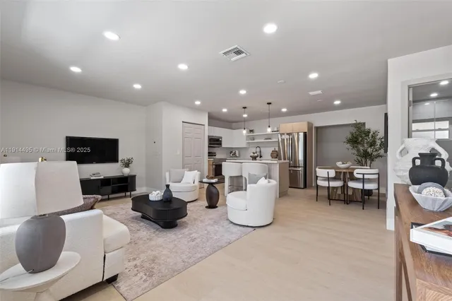 a living room with a white couches and a dining table with wooden floor
