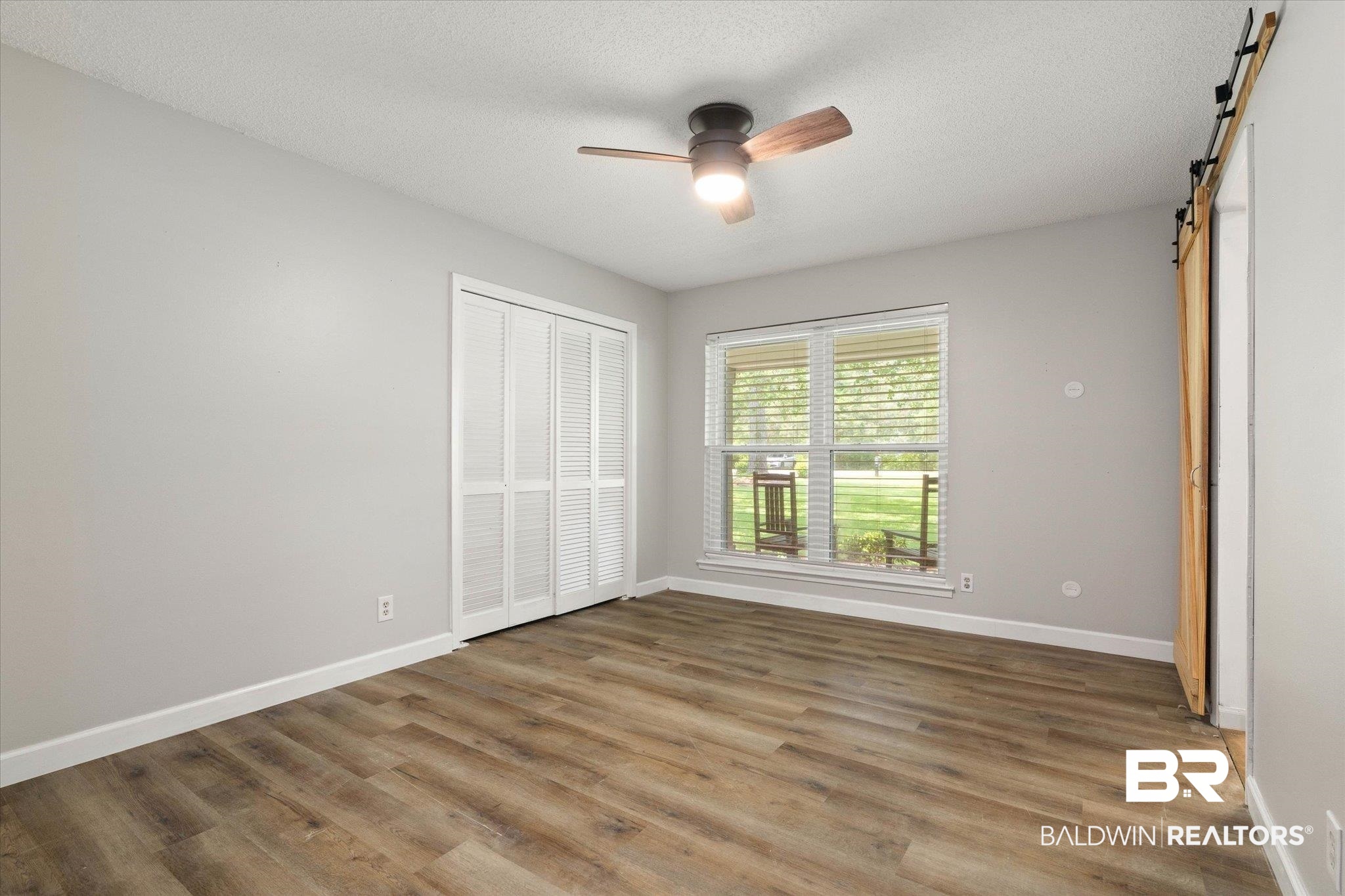 1025 Walter Smith Road Mobile, AL 36695 - Photo 23 of 46 Unfurnished bedroom featuring a barn door, wood finished floors, baseboards, a closet, and a textured ceiling