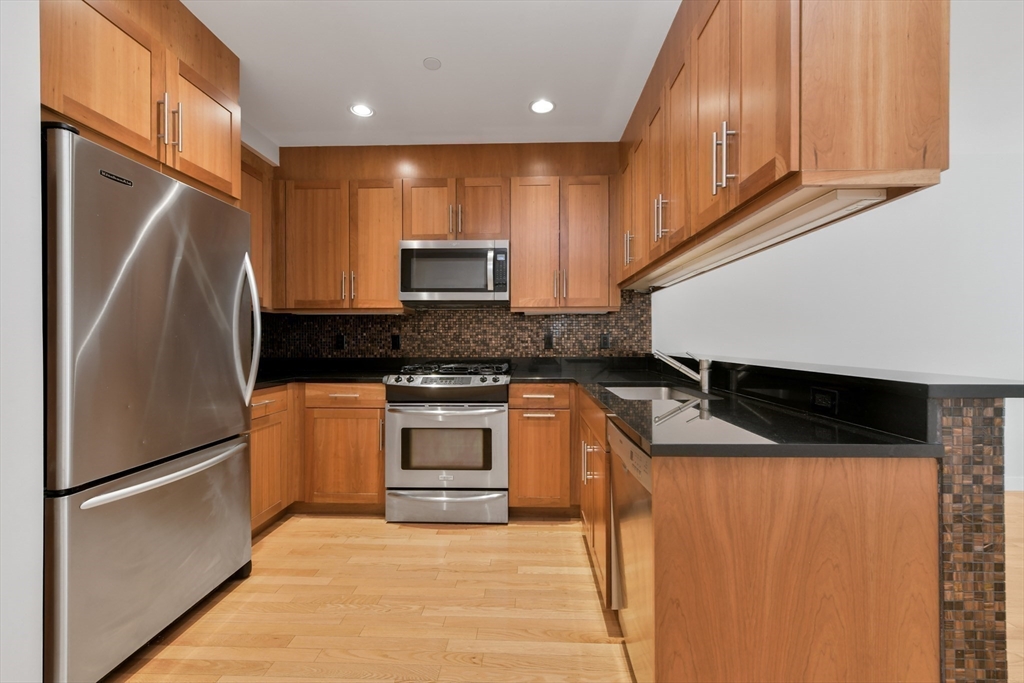 80 Broad Street, Unit 603 Boston, MA 02110 - Photo 5 of 16 a kitchen with stainless steel appliances granite countertop a refrigerator a stove and a sink with wooden cabinets