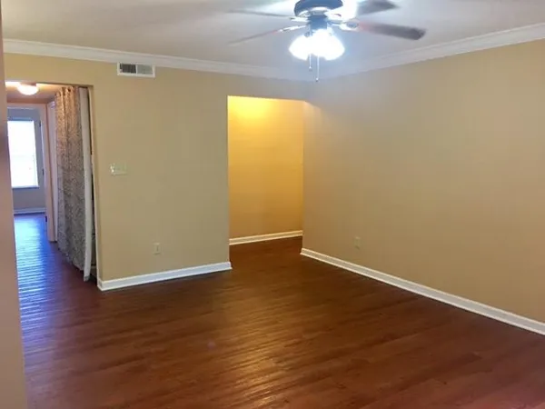 a view of an empty room with wooden floor and a chandelier fan