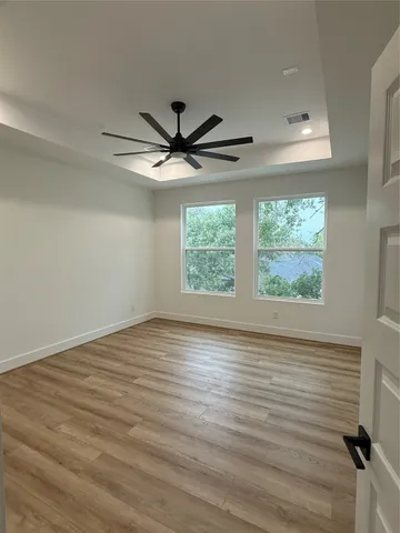 an empty room with wooden floor windows and ceiling fan