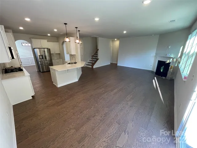 a open kitchen with kitchen island a refrigerator stove a sink and a dining table with wooden floor