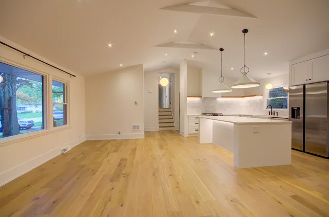 a kitchen with stainless steel appliances granite countertop a refrigerator a oven a sink and white cabinets with wooden floor