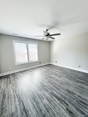an empty room with wooden floor chandelier fan and windows