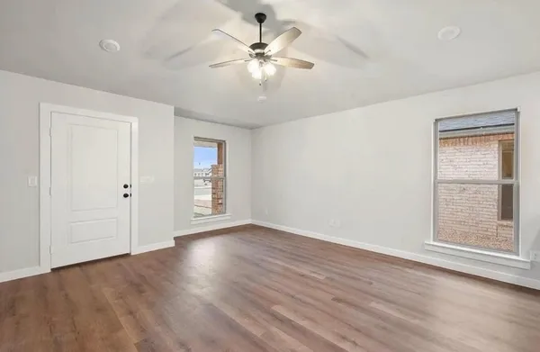 an empty room with wooden floor chandelier fan and windows