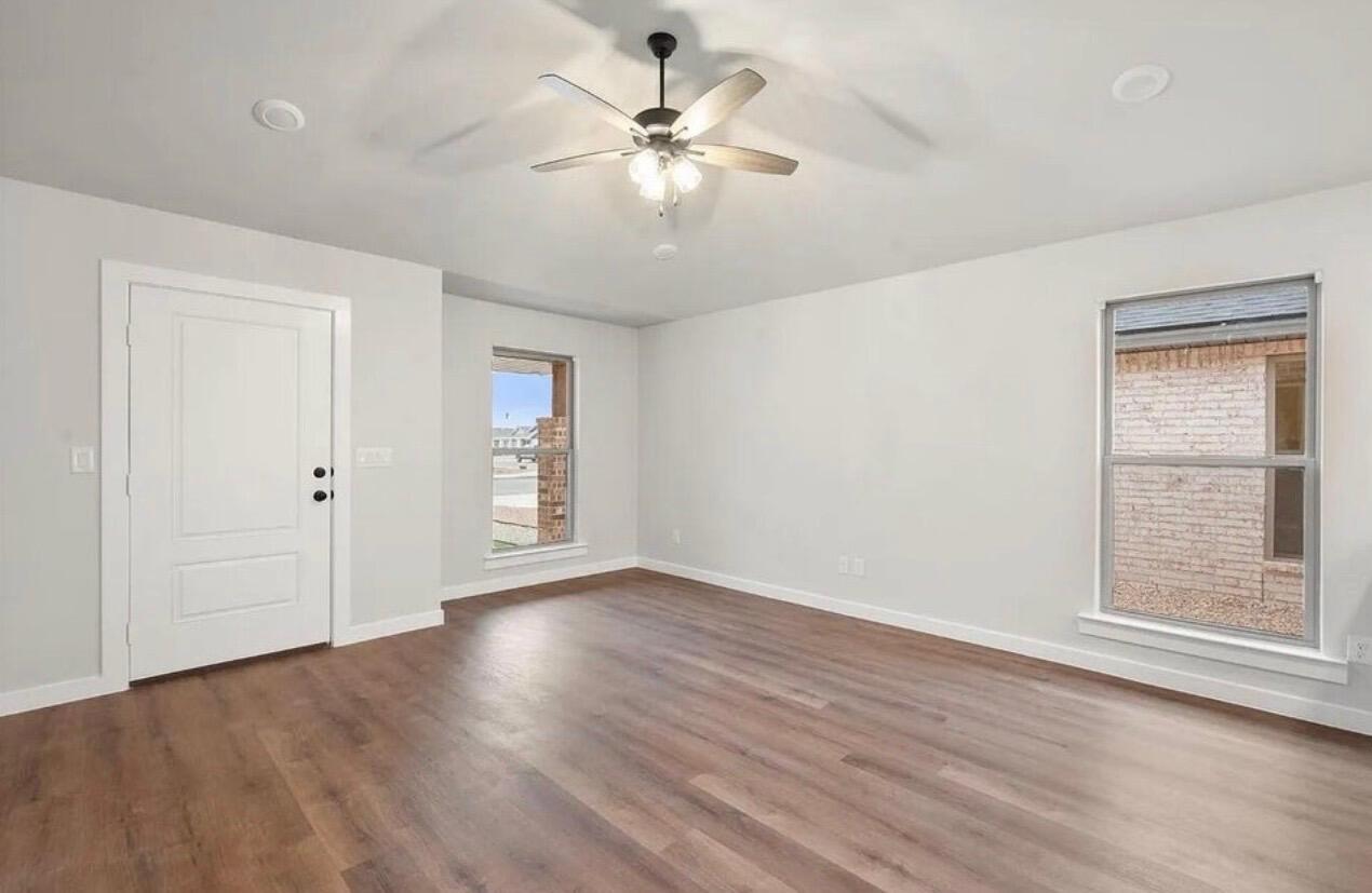 1708 145th Street Lubbock, TX 79423 - Photo 5 of 19 an empty room with wooden floor chandelier fan and windows