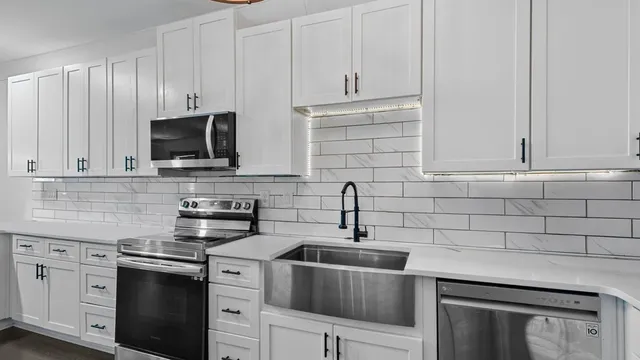 a kitchen with stainless steel appliances granite countertop white cabinets a sink a stove and dishwasher