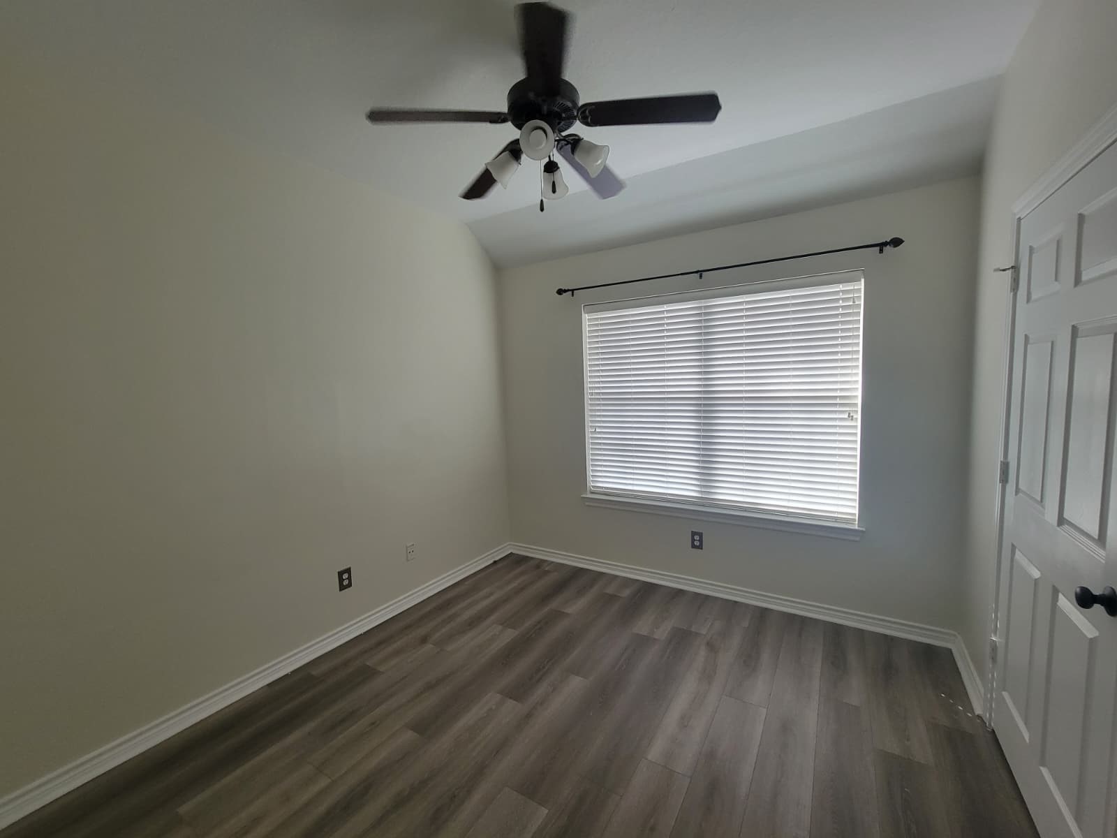 Bright and inviting bedroom featuring sleek laminate flooring, a modern ceiling fan, and ample natural light through large windows with blinds.