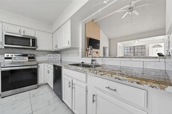 a kitchen with granite countertop a sink stainless steel appliances and white cabinets