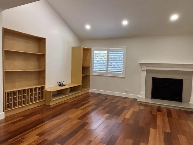 an empty room with wooden floor fireplace and windows