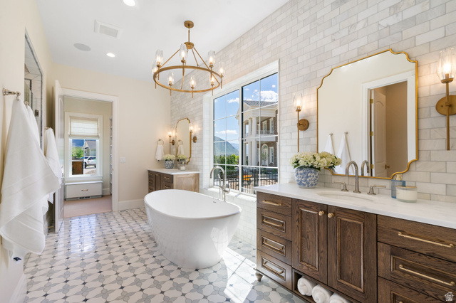 115 East Hidden Ridge Lane, Unit 42 Mapleton, UT 84664 - Photo 27 of 103 Freestanding soaking tub with patterned floor tiling, twin dark wood vanities featuring light stone countertops, and a full-height window