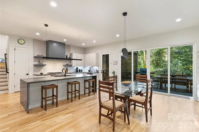 a kitchen with stainless steel appliances granite countertop a stove top oven a sink a dining table and chairs with wooden floor