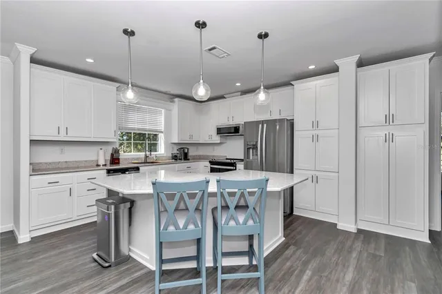 a kitchen with stainless steel appliances kitchen island granite countertop a wooden floor and white cabinets